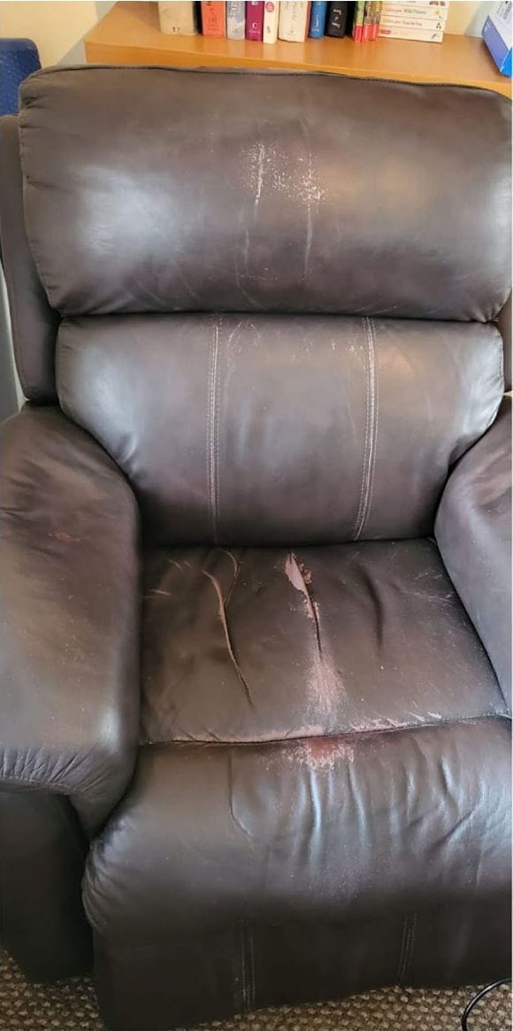 Brown leather recliner armchair with a torn seat panel and worn headrest before repair